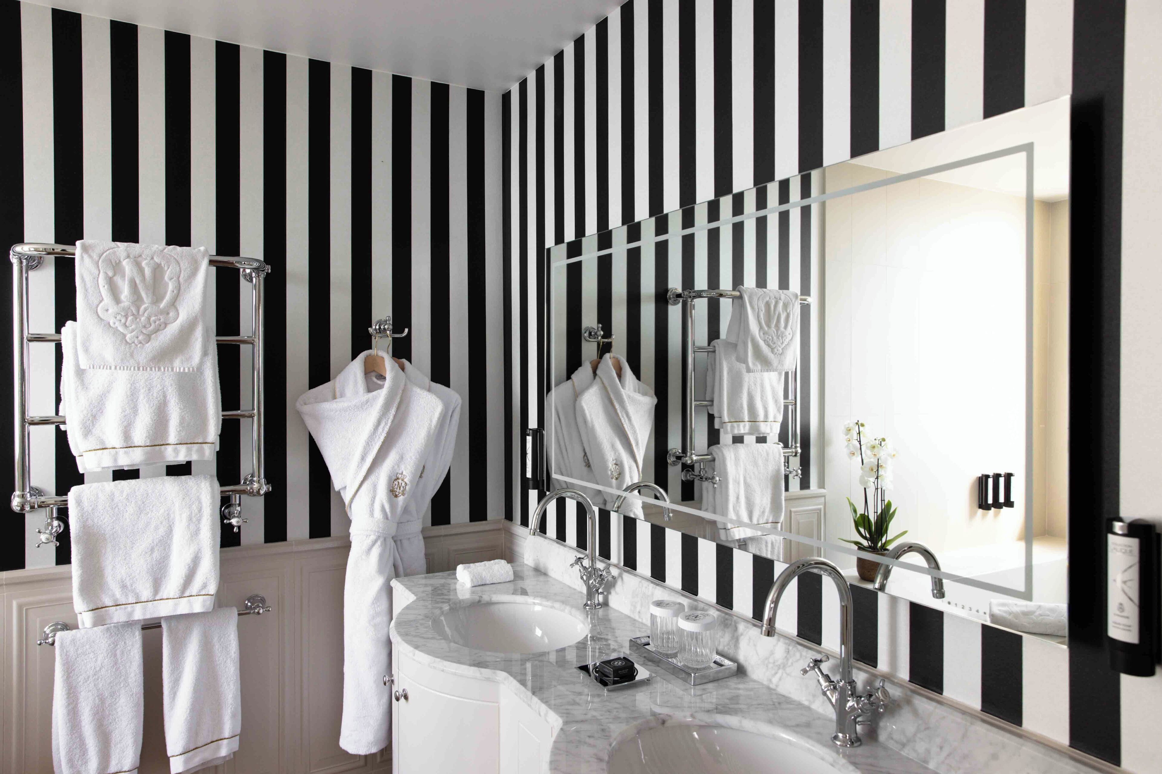 A bathroom with a black and white striped wall, a large mirror, a sink, and multiple towels on towel racks.
