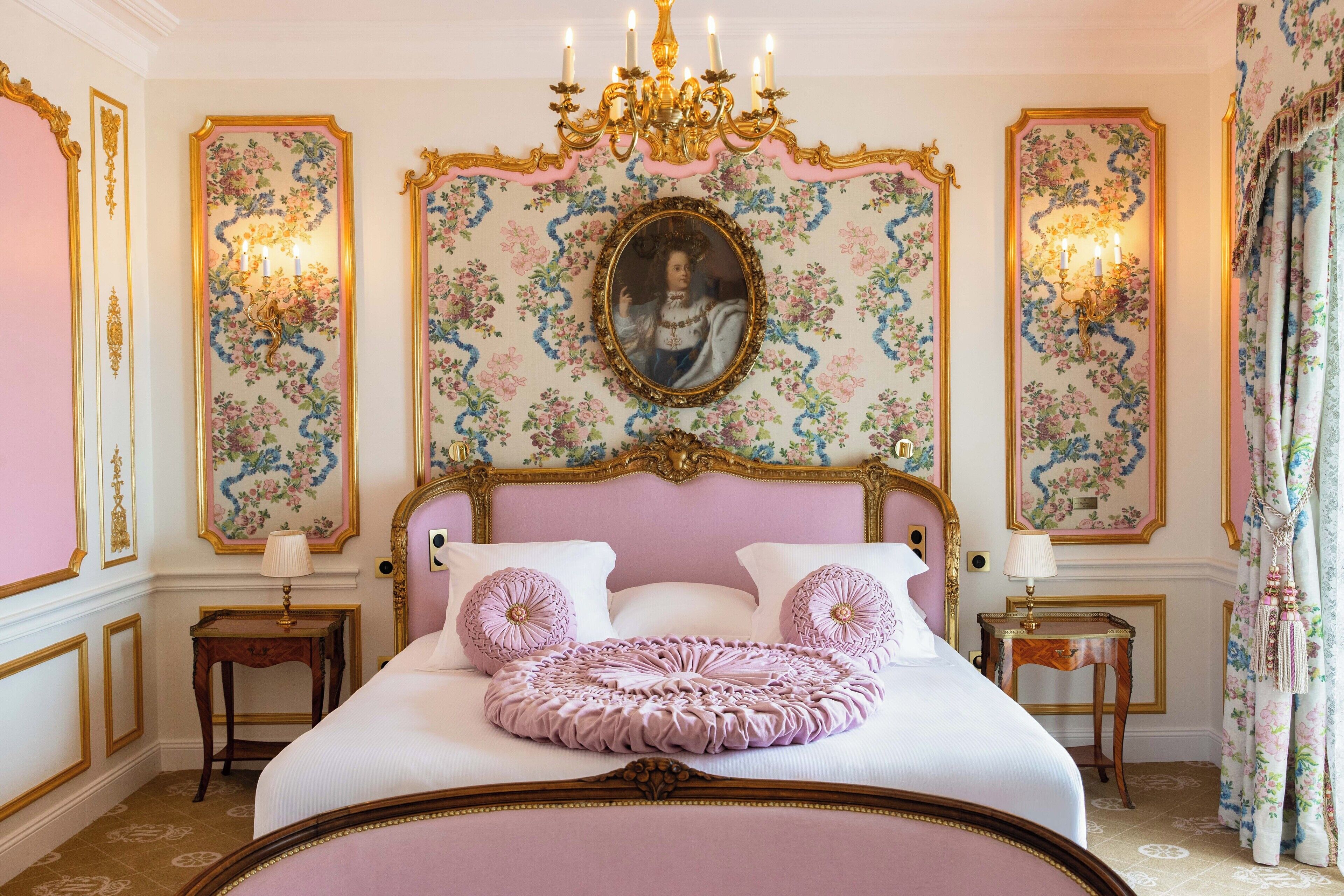 Un dormitorio lujoso con una cama grande, un cabecero ornamentado, papel tapiz floral y decoración clásica.
