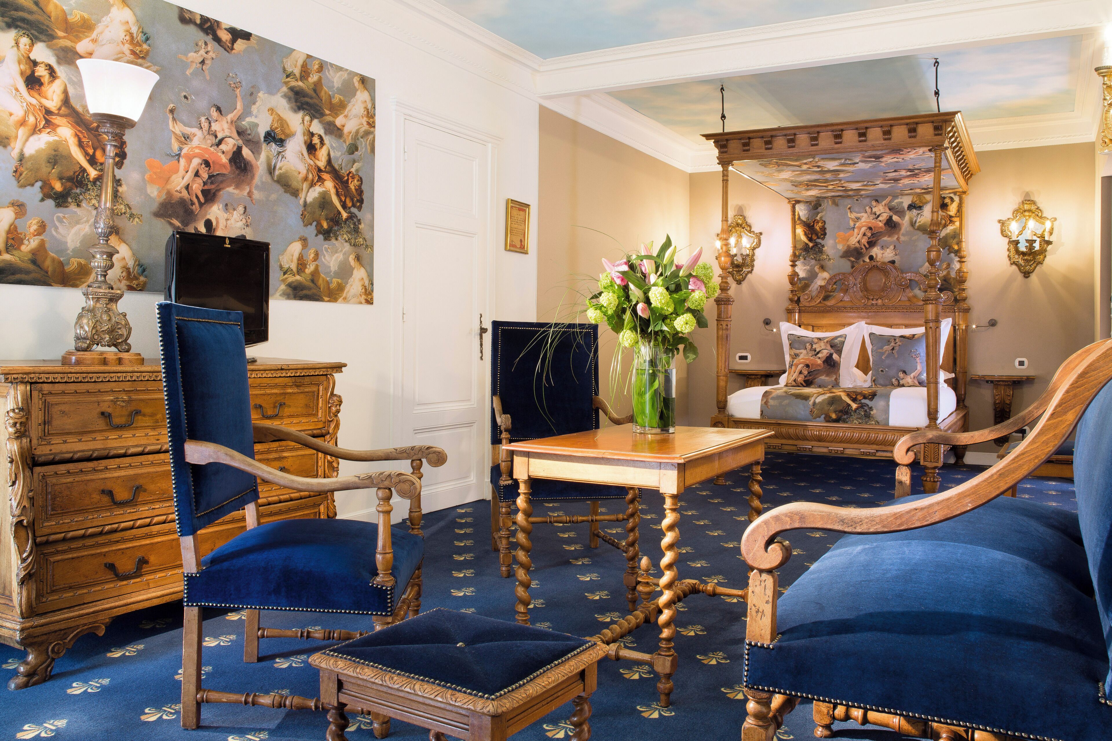 A room with a classic design, featuring a large ornate bed, a wooden dresser, and a blue upholstered chair.