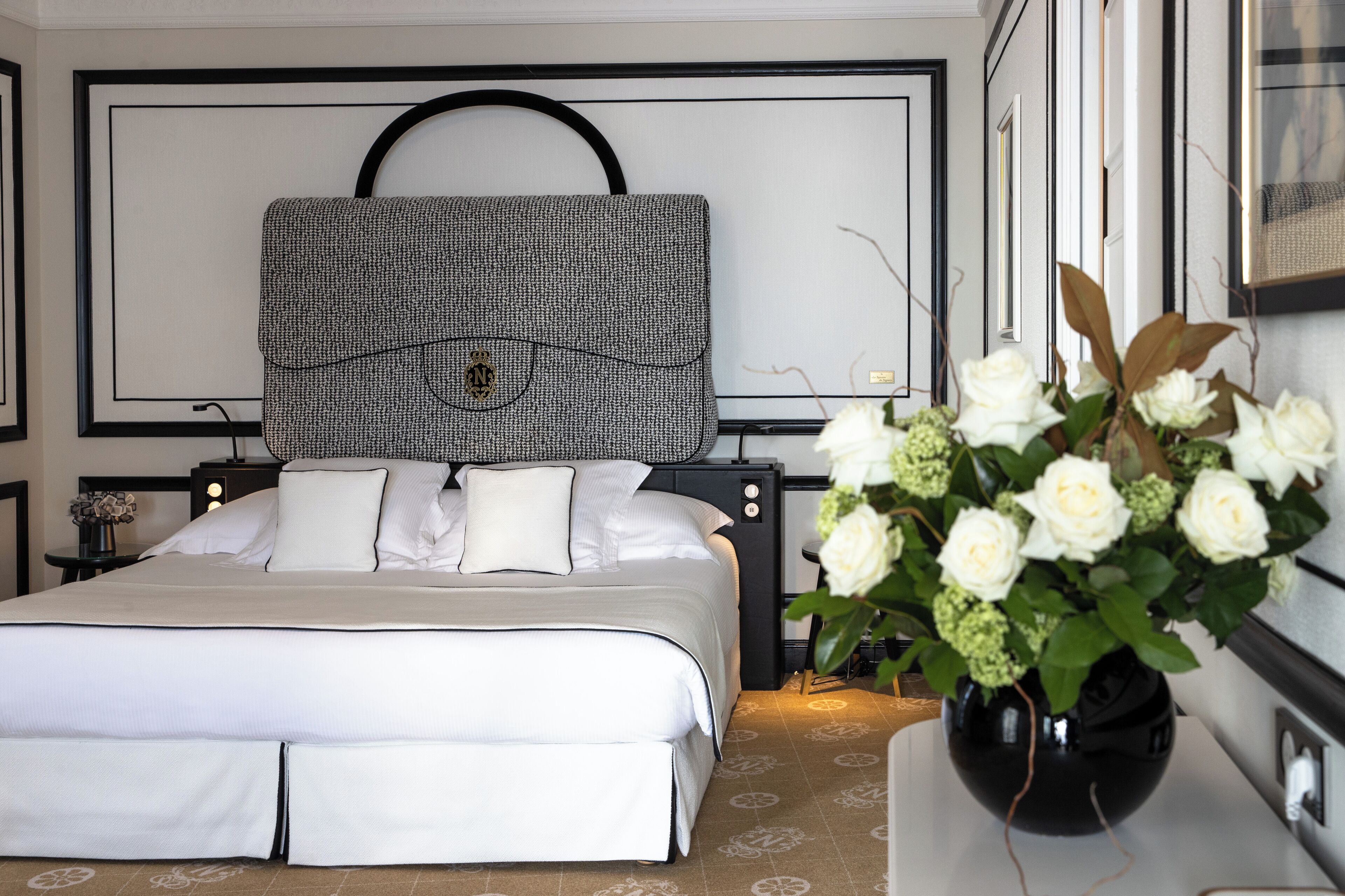 Een keurig opgeruimde hotelkamer met een groot bed, een hoofdbord met een patroon, een nachtkastje met een bloevas en een tv aan de muur.