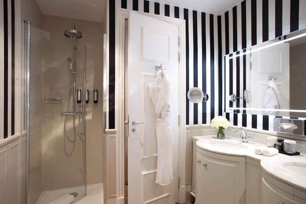 A bathroom with a glass-enclosed shower, a white vanity with a mirror, and a white towel hanging on the door.