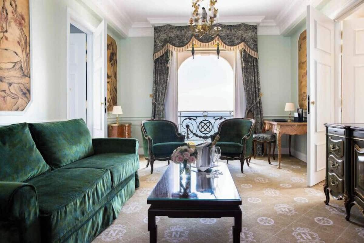 A room with a green sofa, a coffee table with a vase, two chairs, a desk, and a chandelier.
