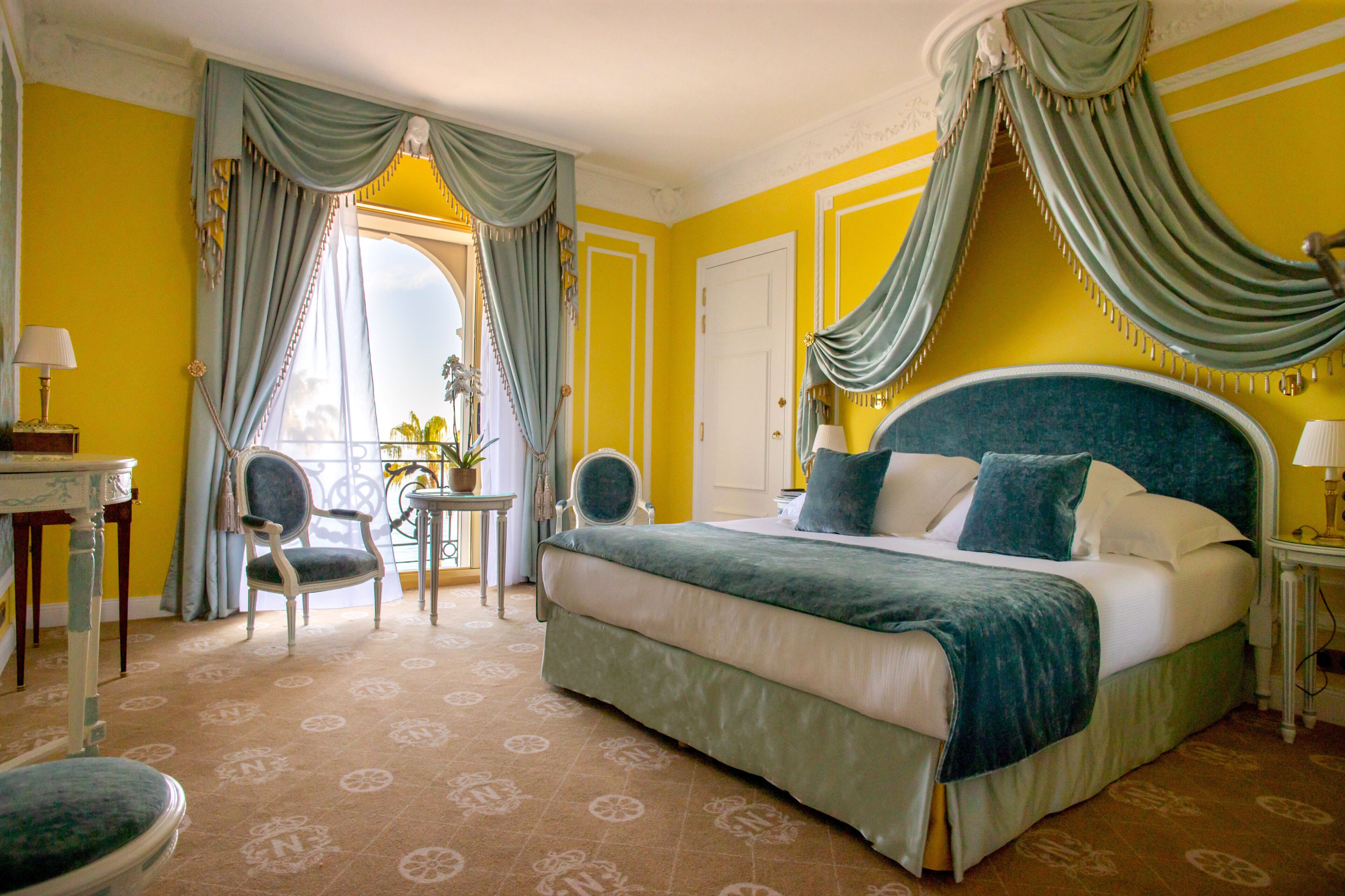 A hotel room with a large bed, a desk, a chair, and a view of the outdoors.