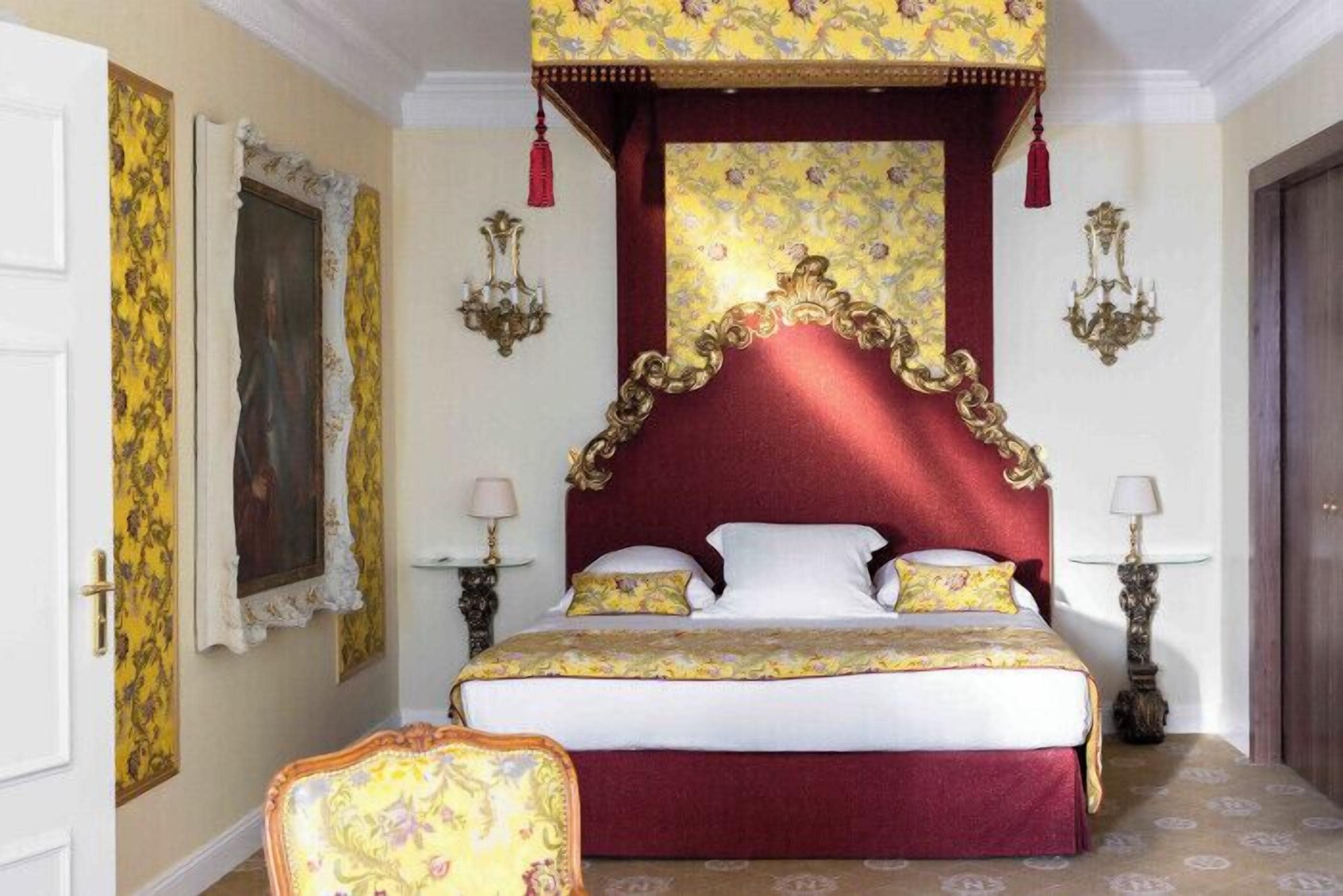 Une chambre à coucher avec un grand lit, une tête de lit décorée, un papier peint à motifs floraux et un décor classique.