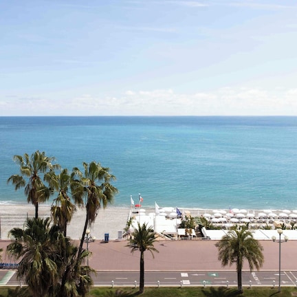 A beachside view with palm trees, a promenade, and a row of umbrellas.