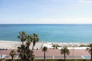 Une vue sur la plage, avec des palmiers, une promenade et une rangée de parasols.