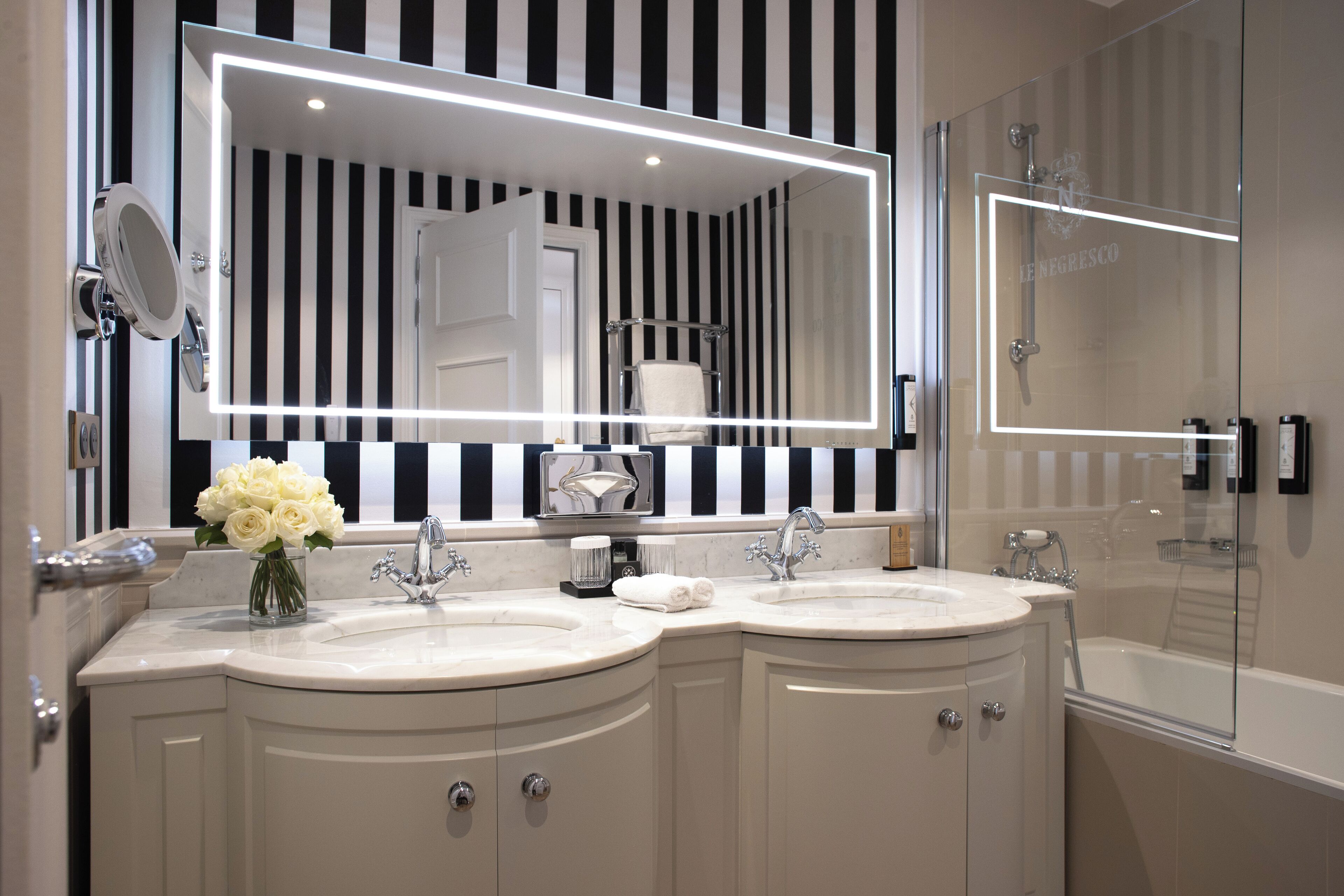 Une salle de bain moderne avec deux lavabos, un grand miroir et une douche à parois de verre.
