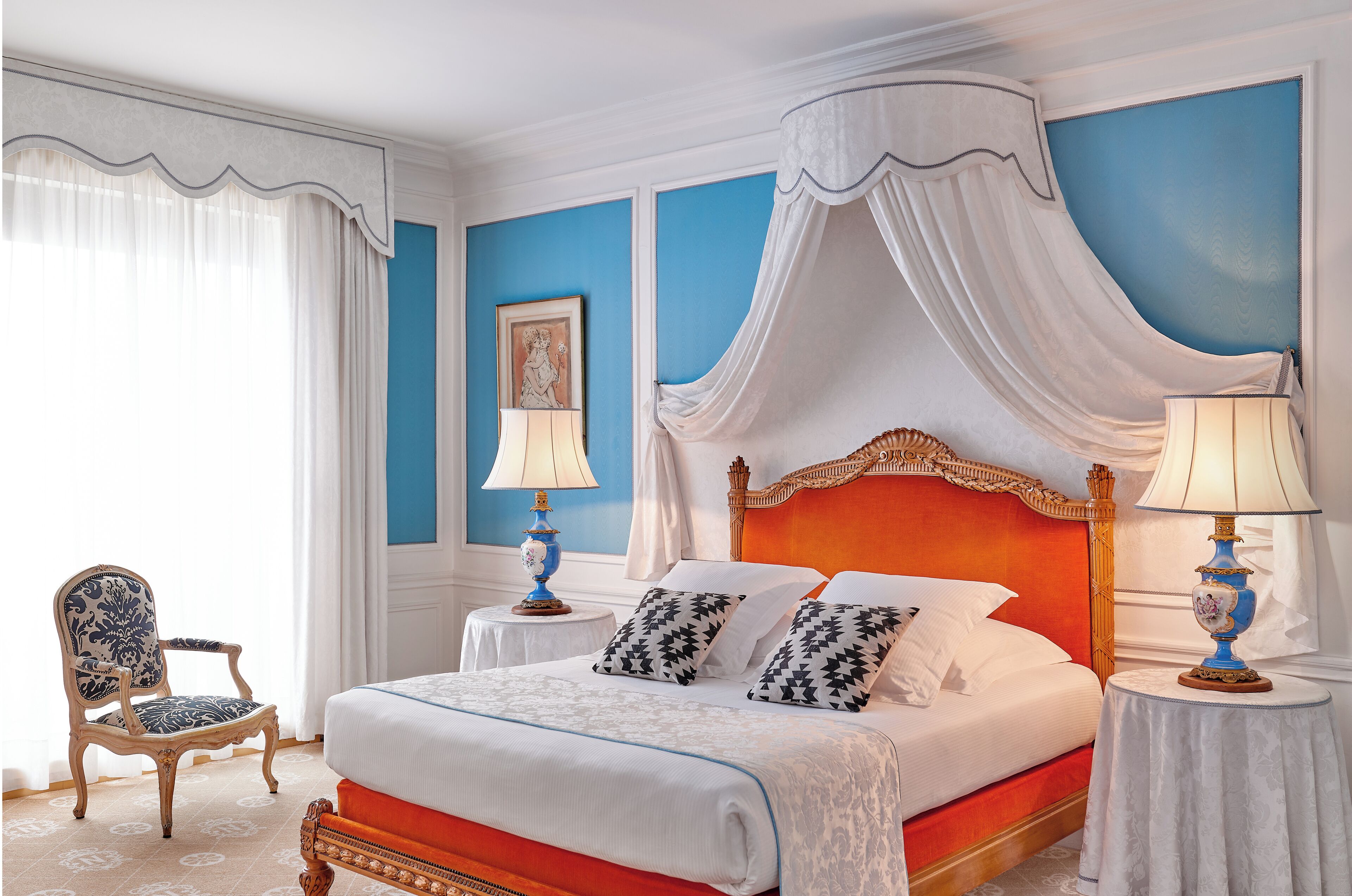 A bedroom with a four-poster bed, a chair, two bedside tables, and a picture on the wall.
