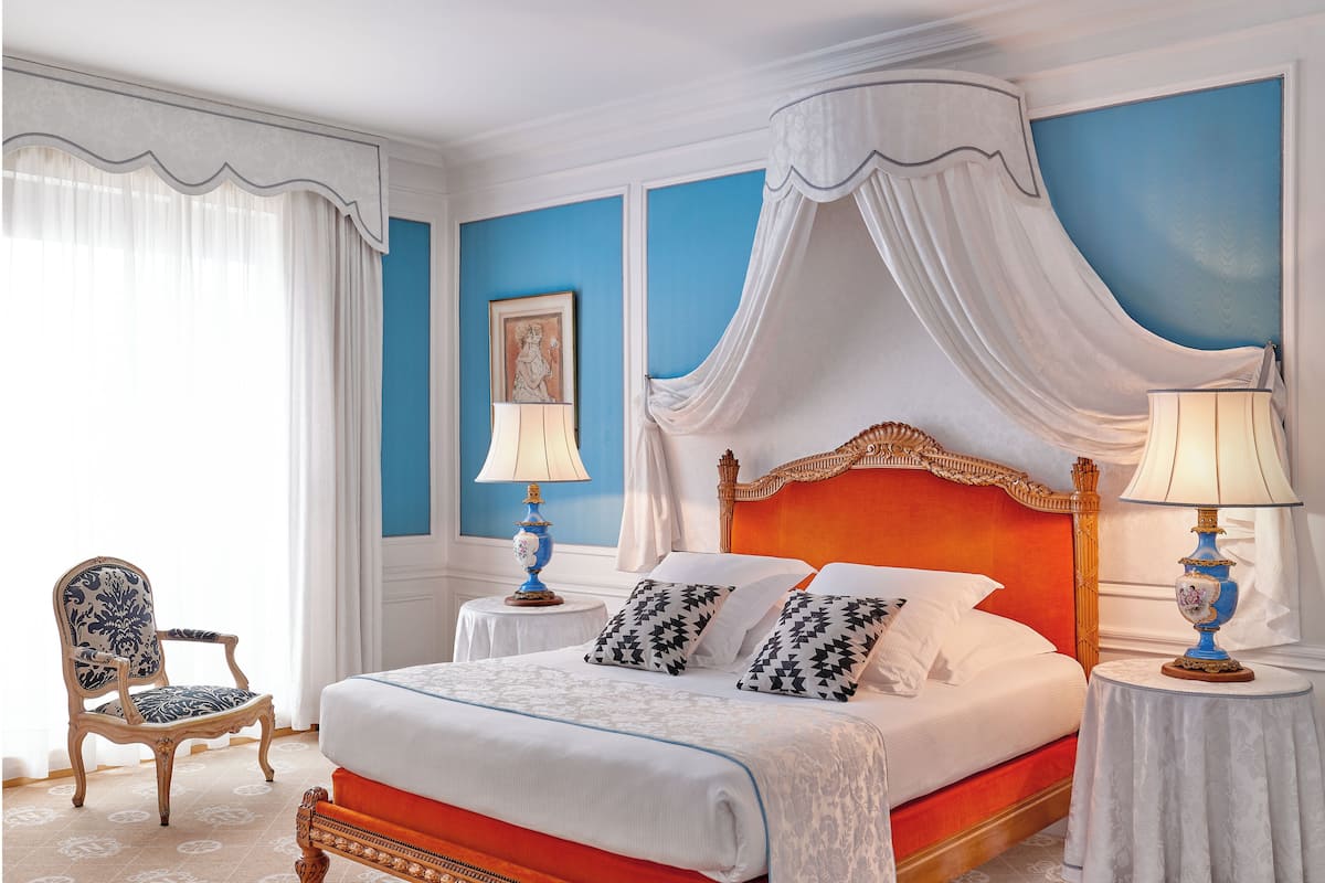 A bedroom with a four-poster bed, a chair, two bedside tables, and a picture on the wall.
