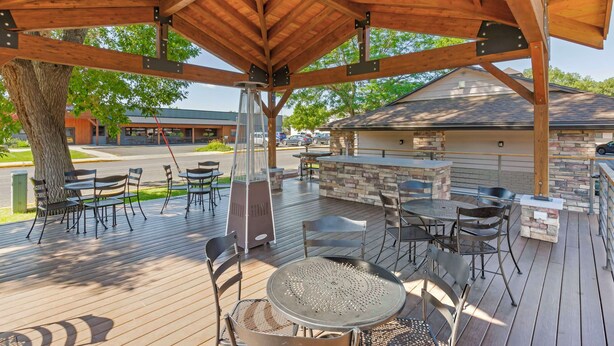 A covered outdoor patio with wooden beams, tables, chairs, and a stone fireplace. - Best Western Sunset Inn (Cody)