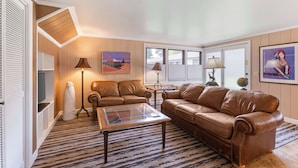 A living room with a brown leather sofa, a glass coffee table, a floor lamp, and a painting on the wall. - Best Western Sunset Inn (Cody)