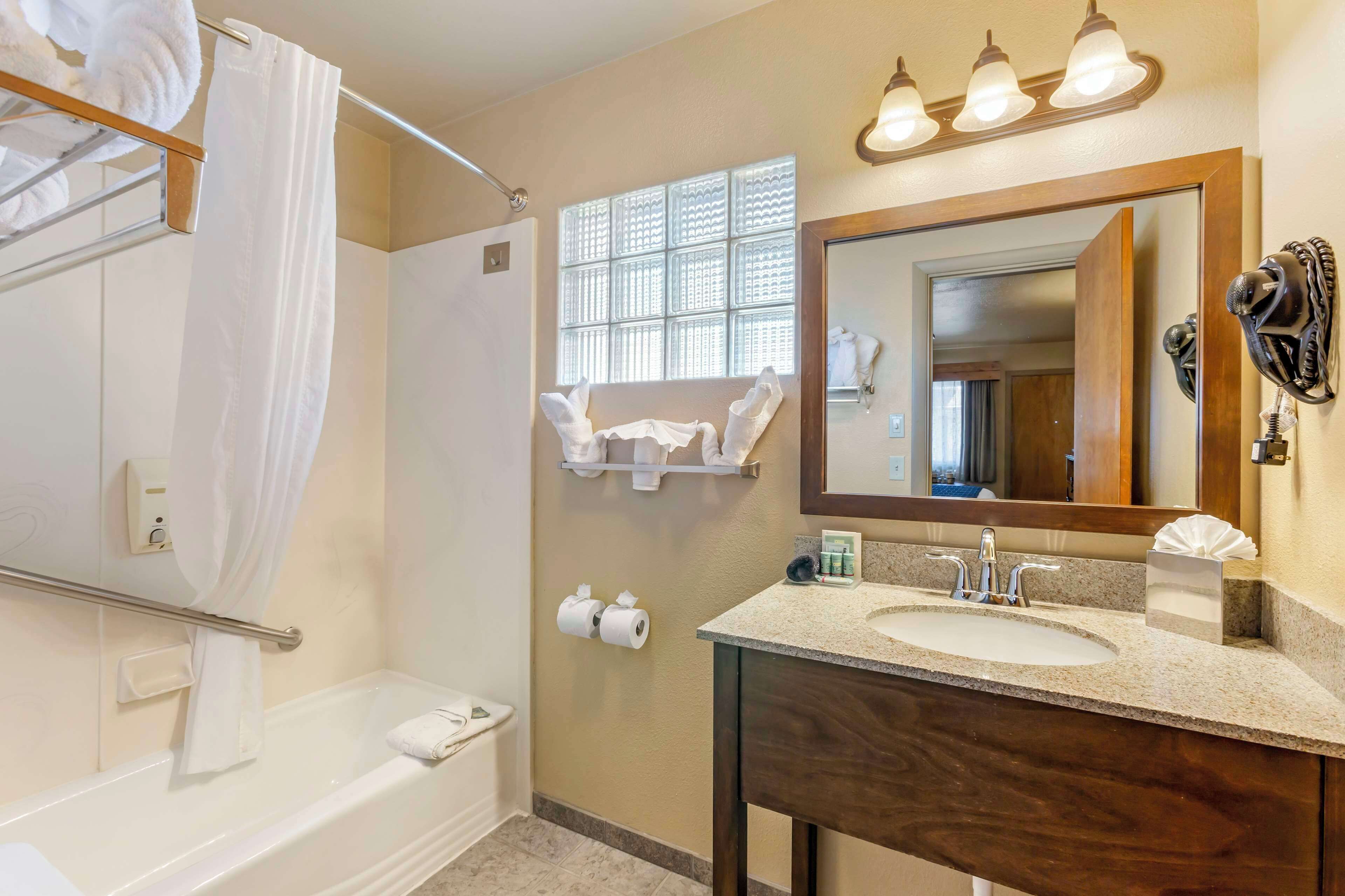 A bathroom with a bathtub, a sink, a mirror, and a window with patterned blinds.