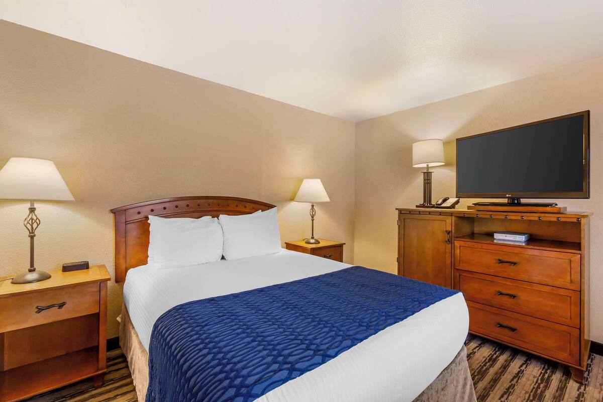 Habitación de hotel con una cama grande, dos mesitas de noche con lámparas, un aparador de madera y un televisor de pantalla plana montado en la pared.