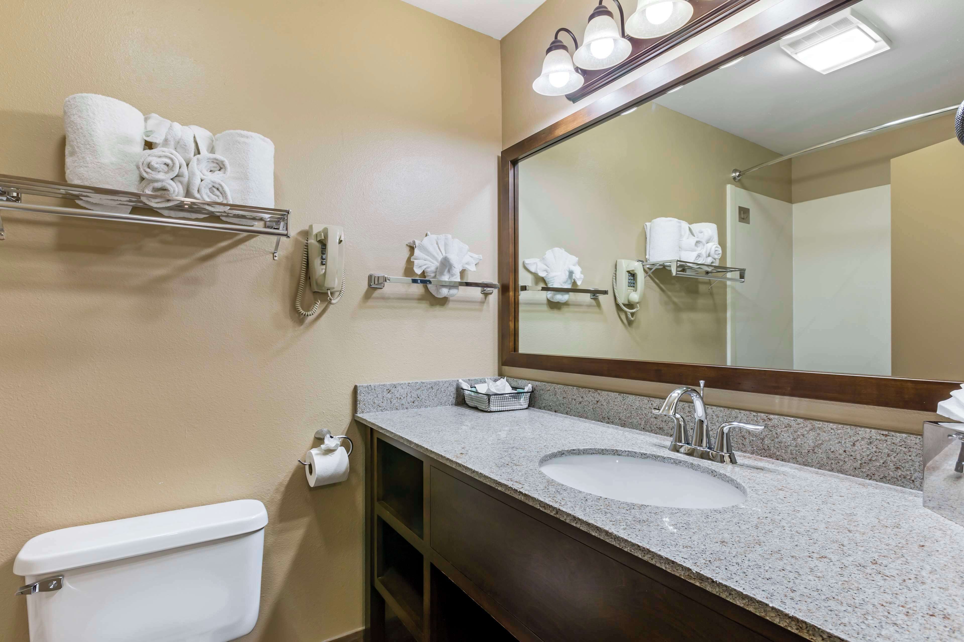 A bathroom with a sink, mirror, towel rack, toilet, and a trash bin.