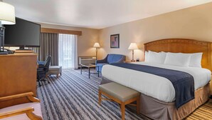 A hotel room with a large bed, a desk with a TV, a chair, a sofa, and a lamp. - Best Western Sunset Inn (Cody)
