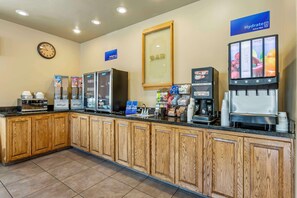 A self-service breakfast area with a clock, beverage dispensers, and a coffee station.