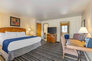 A hotel room with a large bed, a desk with a chair, a television, and a dresser.