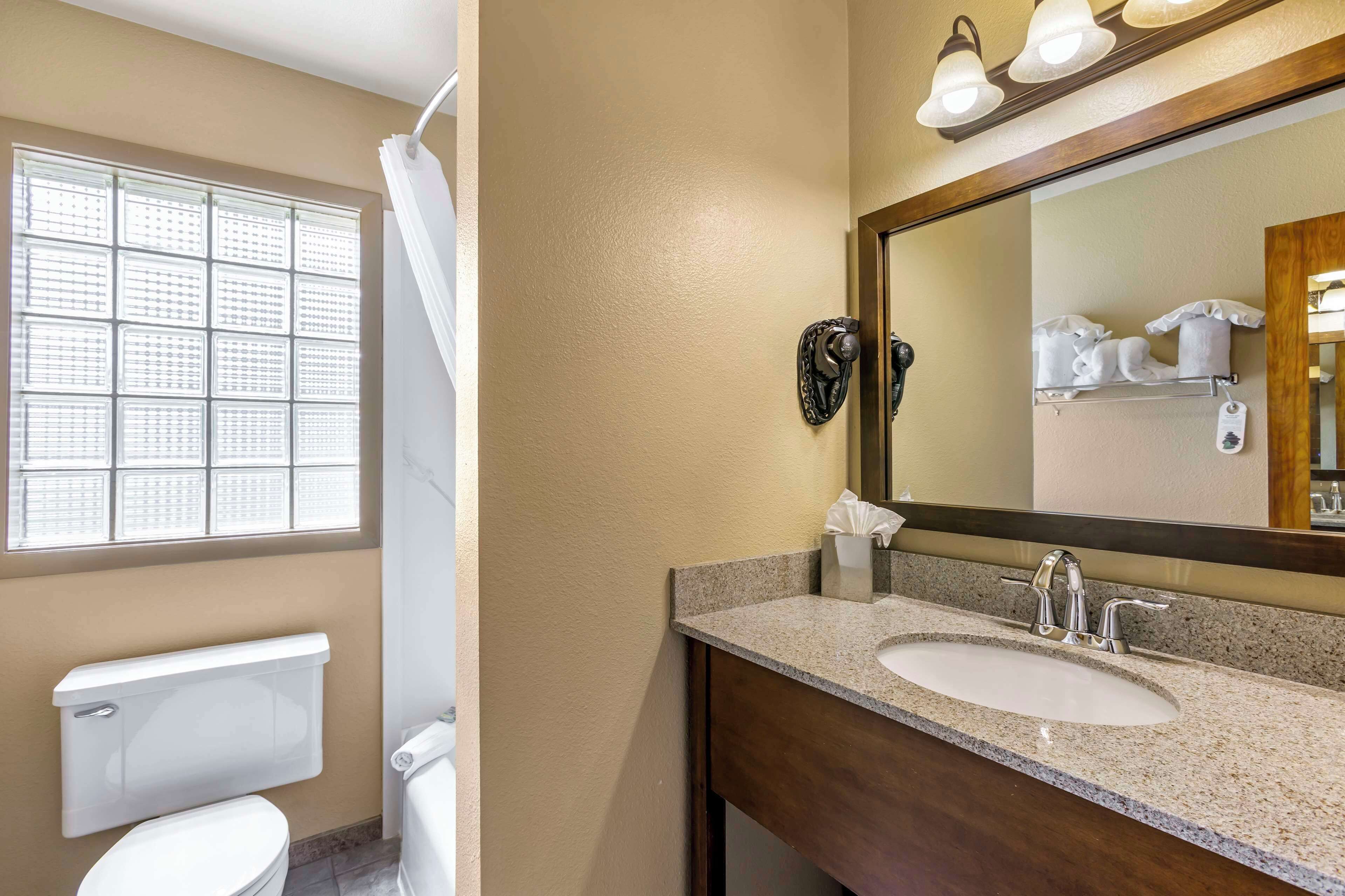 A bathroom with a toilet, a sink, a mirror, and a window with blinds.