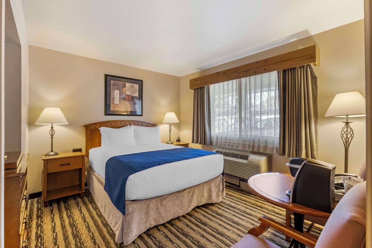 Una habitación de hotel con cama, mesitas de noche, un escritorio y una silla.