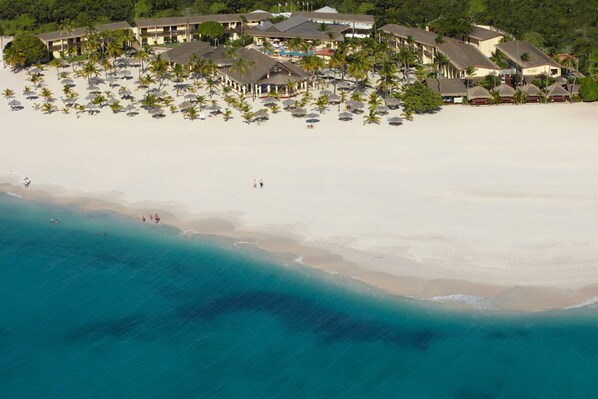 An aerial view of a beachfront hotel with multiple buildings, a sandy beach, and numerous umbrellas. - Manchebo Beach Resort and Spa (Oranjestad)