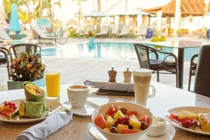 A breakfast table with a pool view, including a fruit bowl, a wrap, and a coffee cup. - Manchebo Beach Resort and Spa (Oranjestad)