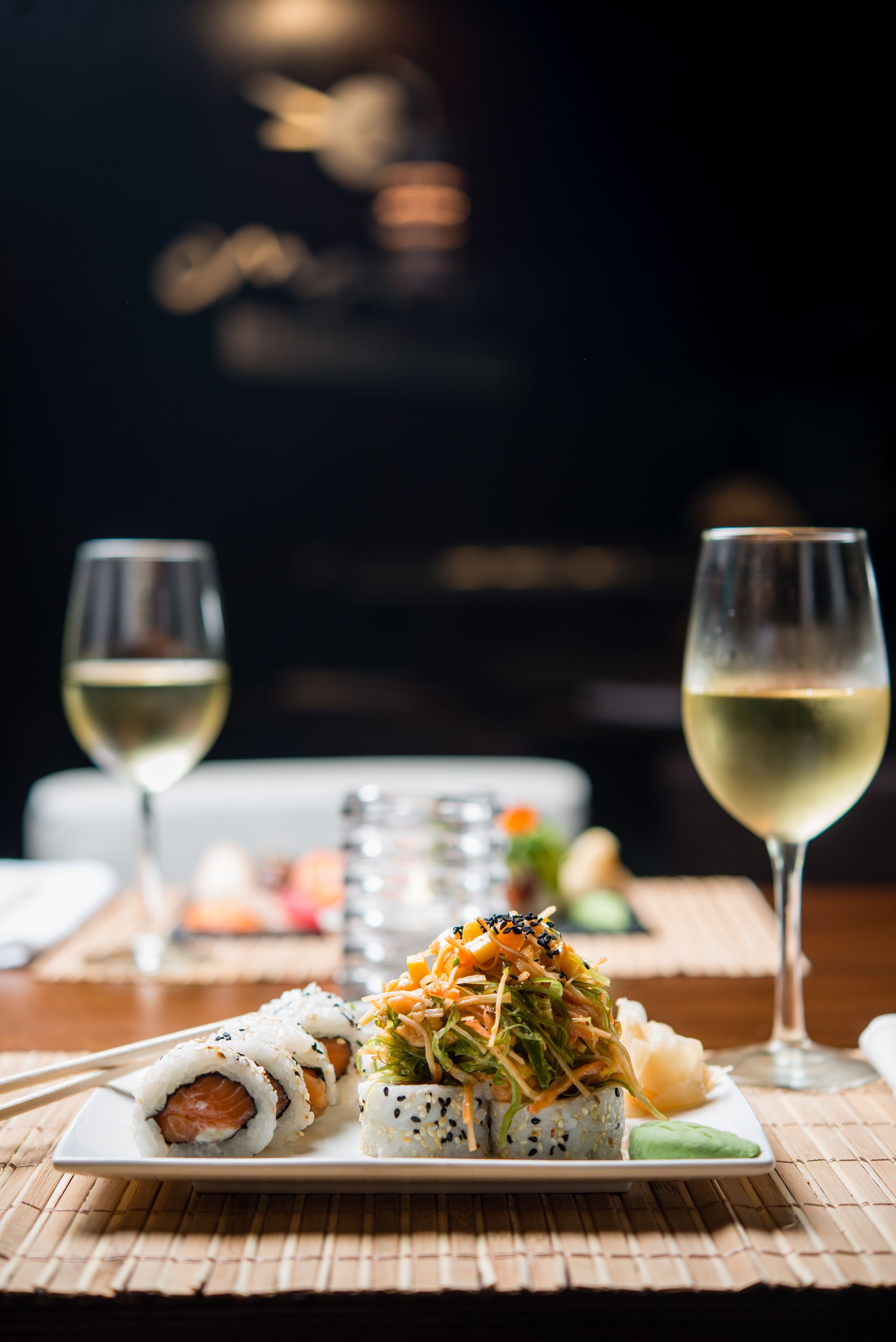 Un plato de sushi con una copa de vino blanco sobre una mesa.