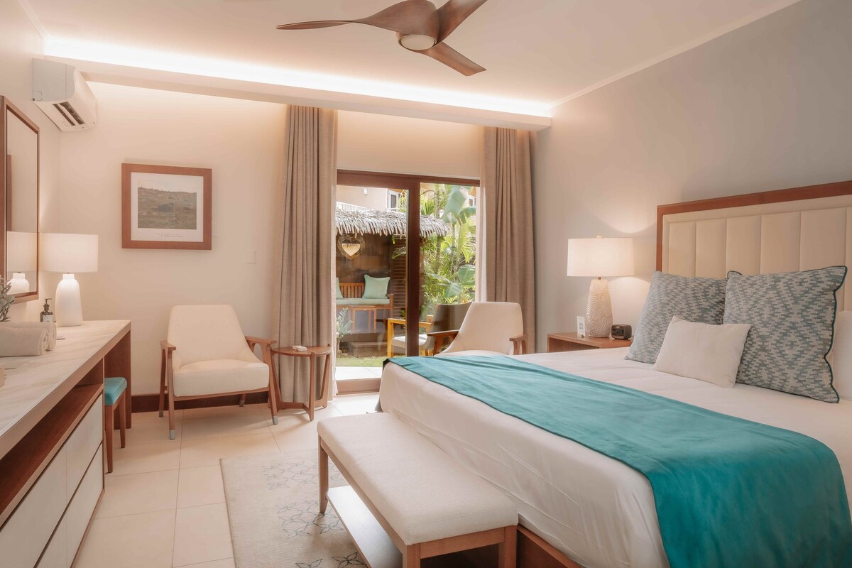 A hotel room with a bed, two chairs, a desk, and a bench.