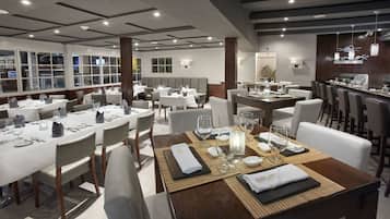 Un restaurante con varias mesas dispuestas para comer, con manteles blancos y cubiertos ordenados.