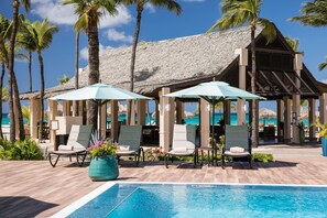 A poolside area with lounge chairs, umbrellas, and a thatched-roof structure. - Manchebo Beach Resort and Spa (Oranjestad)
