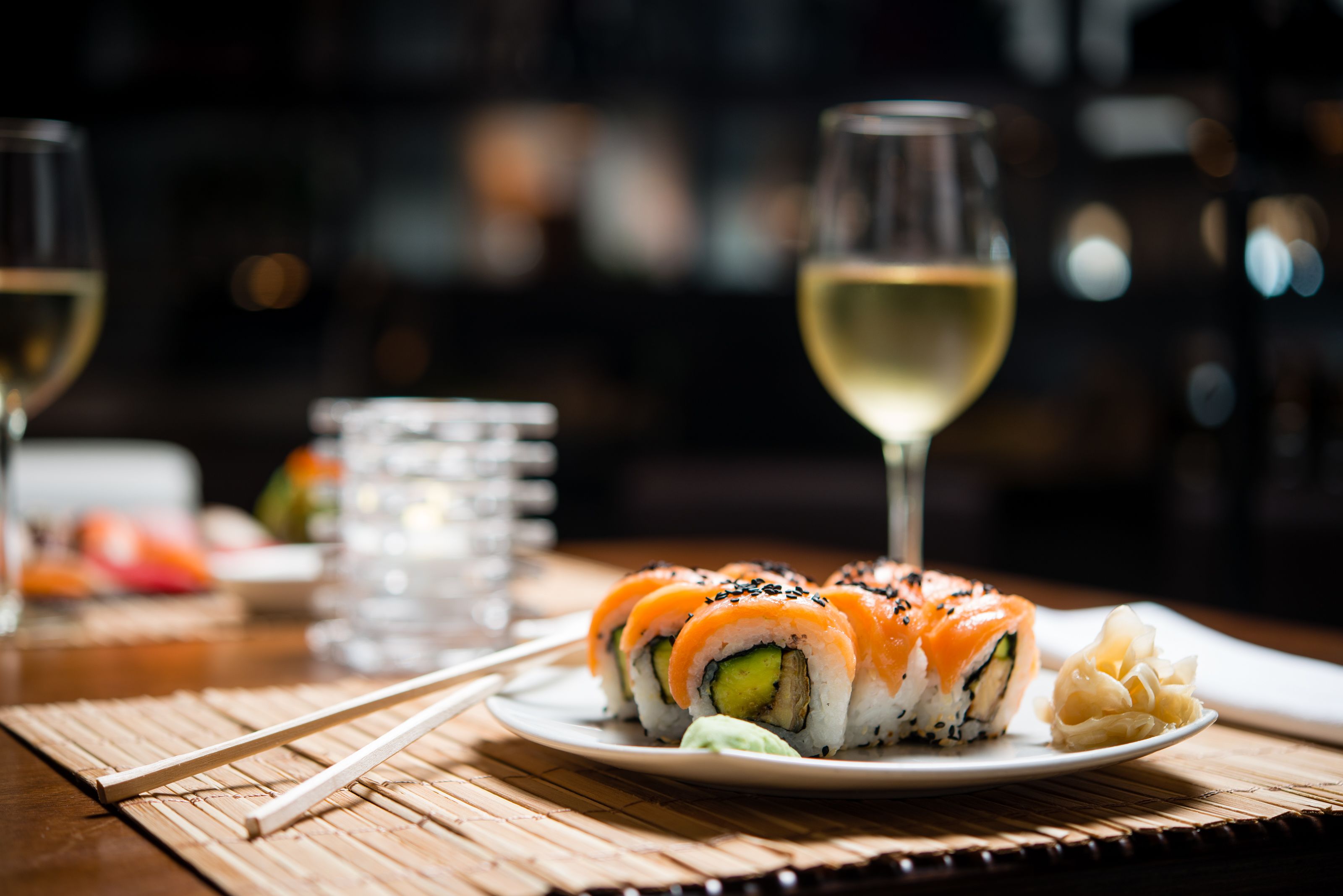 Un plato de sushi con una copa de vino blanco sobre una mesa de madera.