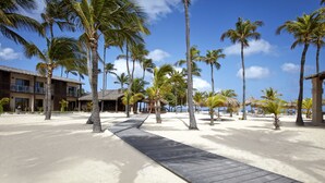 Un resort con playa de arena, palmeras y un paseo marítimo de madera.