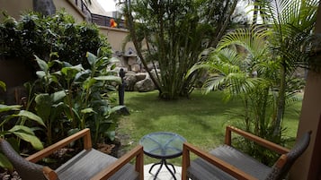 En terrasse med to fletstole, et lille rundt bord og frodig, tropisk vegetation.