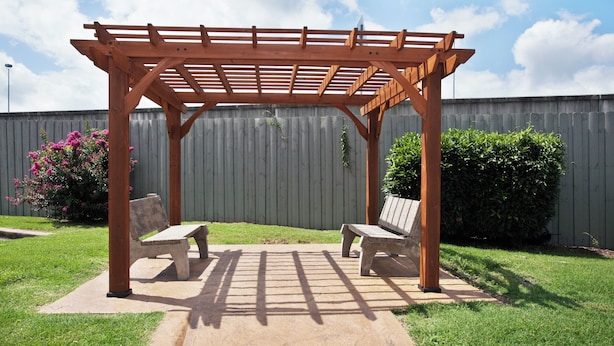 Uma pérgola de madeira com dois bancos num quintal.
