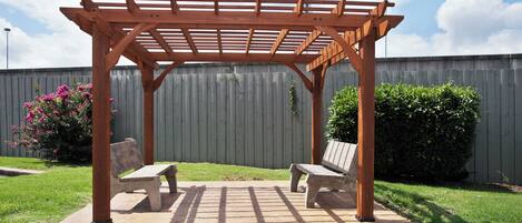 A wooden pergola with two benches in a backyard.