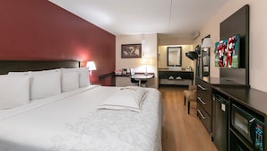 Quarto de hotel com uma cama grande, uma escrivaninha, uma cadeira, televisão, espelho e banheiro.