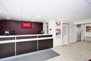 A reception area with a digital screen displaying 'Free Wi-Fi All Rooms,' a reception desk, a security intercom, and an elevator. - Red Roof Inn PLUS+ Nashville South - Fairgrounds (Nashville)