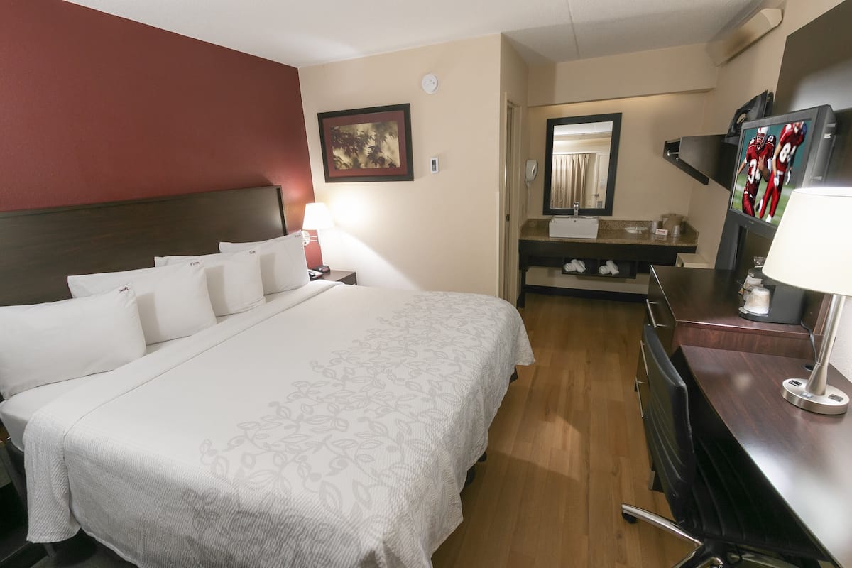 A hotel room with a large bed, a desk, a mirror, and a television.