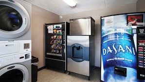 Lavanderia com máquina de lavar, máquina de vendas automática, frigorífico e dispensador de água Dasani.