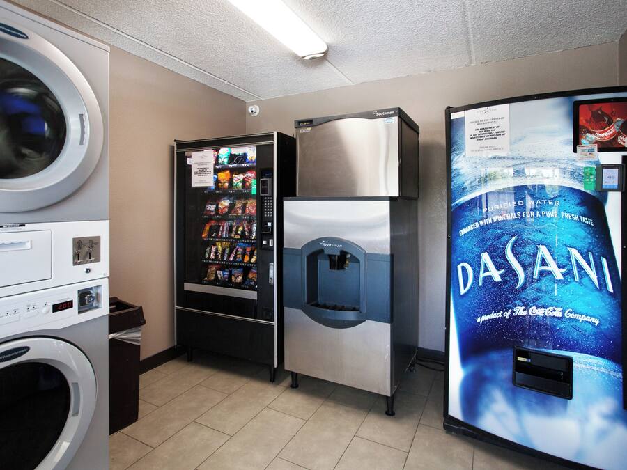 A laundromat with a washing machine, a vending machine, a refrigerator, and a Dasani water dispenser.