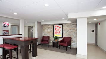 A reception area with a Red Roof Plus sign, a reception desk, two red chairs, and a small table with a plant.