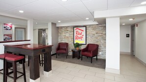 A reception area with a Red Roof Plus sign, a reception desk, two red chairs, and a small table with a plant.
