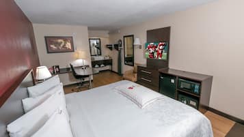 A hotel room with a bed, desk, chair, TV, and a microwave.