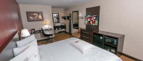 A hotel room with a bed, desk, chair, TV, and a microwave.