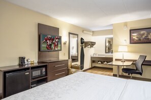 Una habitación de hotel con cama, escritorio, silla, televisión, microondas y refrigerador pequeño.