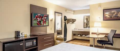 Habitación de hotel con cama, televisión, escritorio, silla, lámpara de escritorio, espejo y cafetera.