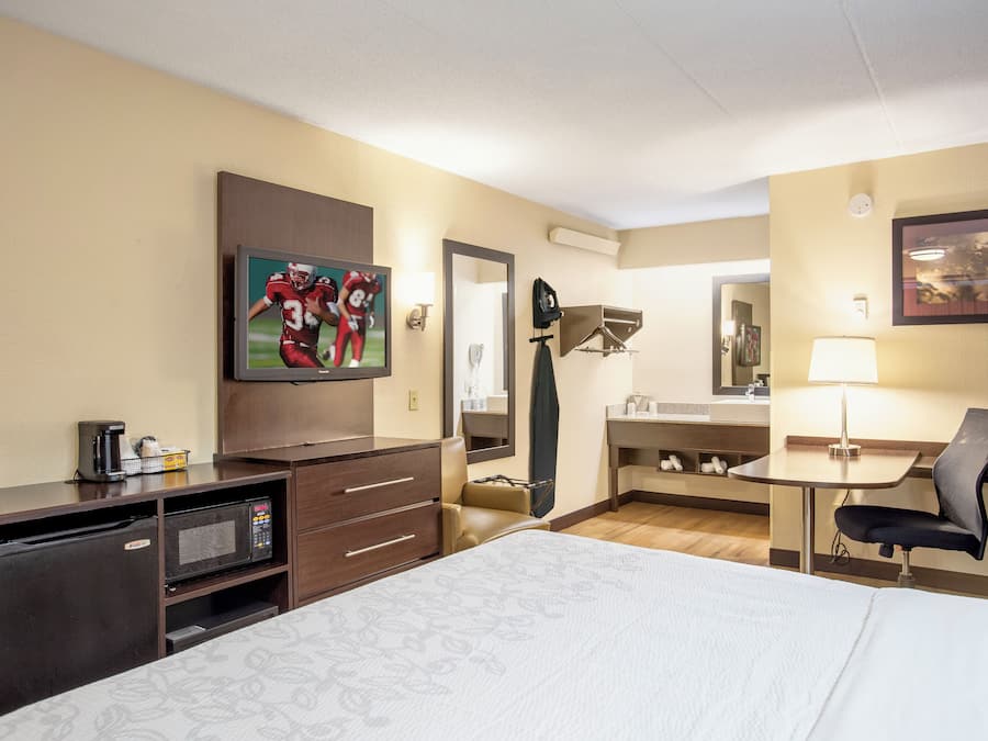 A hotel room with a bed, a TV, a desk, a chair, a desk lamp, a mirror, and a coffee maker.