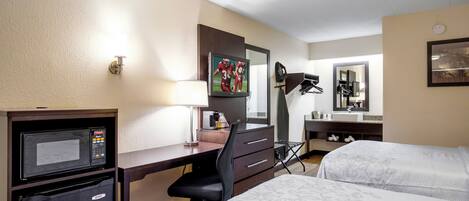 A hotel room with a desk, a television, a bed, a mirror, and a coffee machine.