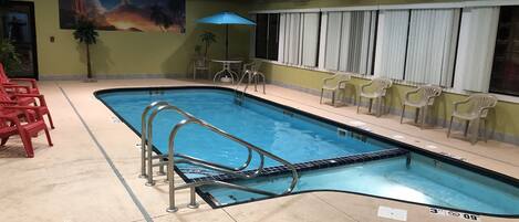Una piscina interior con una escalera de metal, sillas rojas y un mural en la pared.