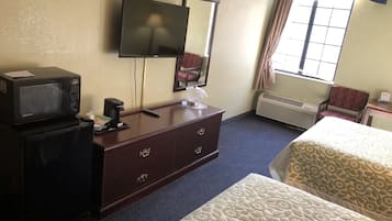 A hotel room with a TV, a desk with a lamp, a mirror, a chair, and two beds.
