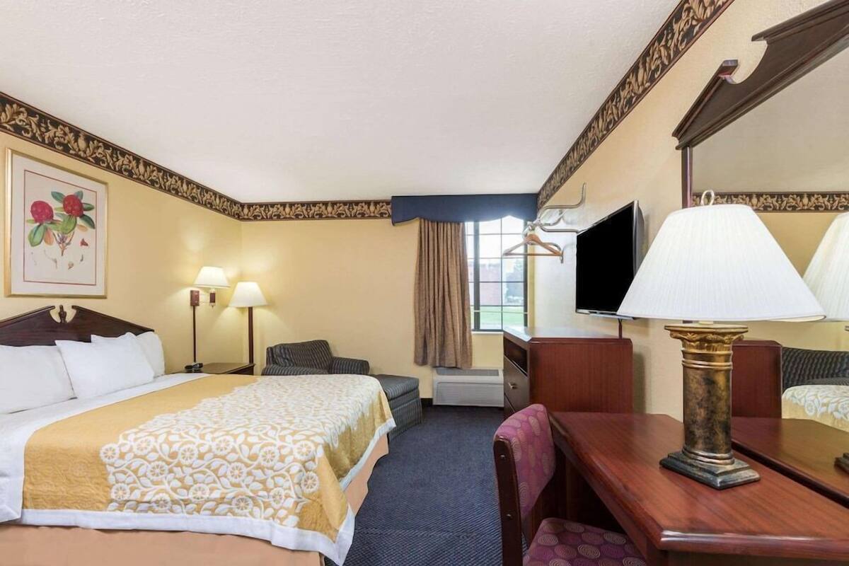 Une chambre d’hôtel avec un lit, un bureau, une chaise, une télévision et une fenêtre avec des rideaux.